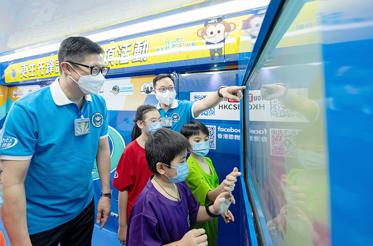 保安局局长邓炳强(左一)及惩教署署长黄国兴(后排右一)与学生在教育宣传车上参与电子游戏。