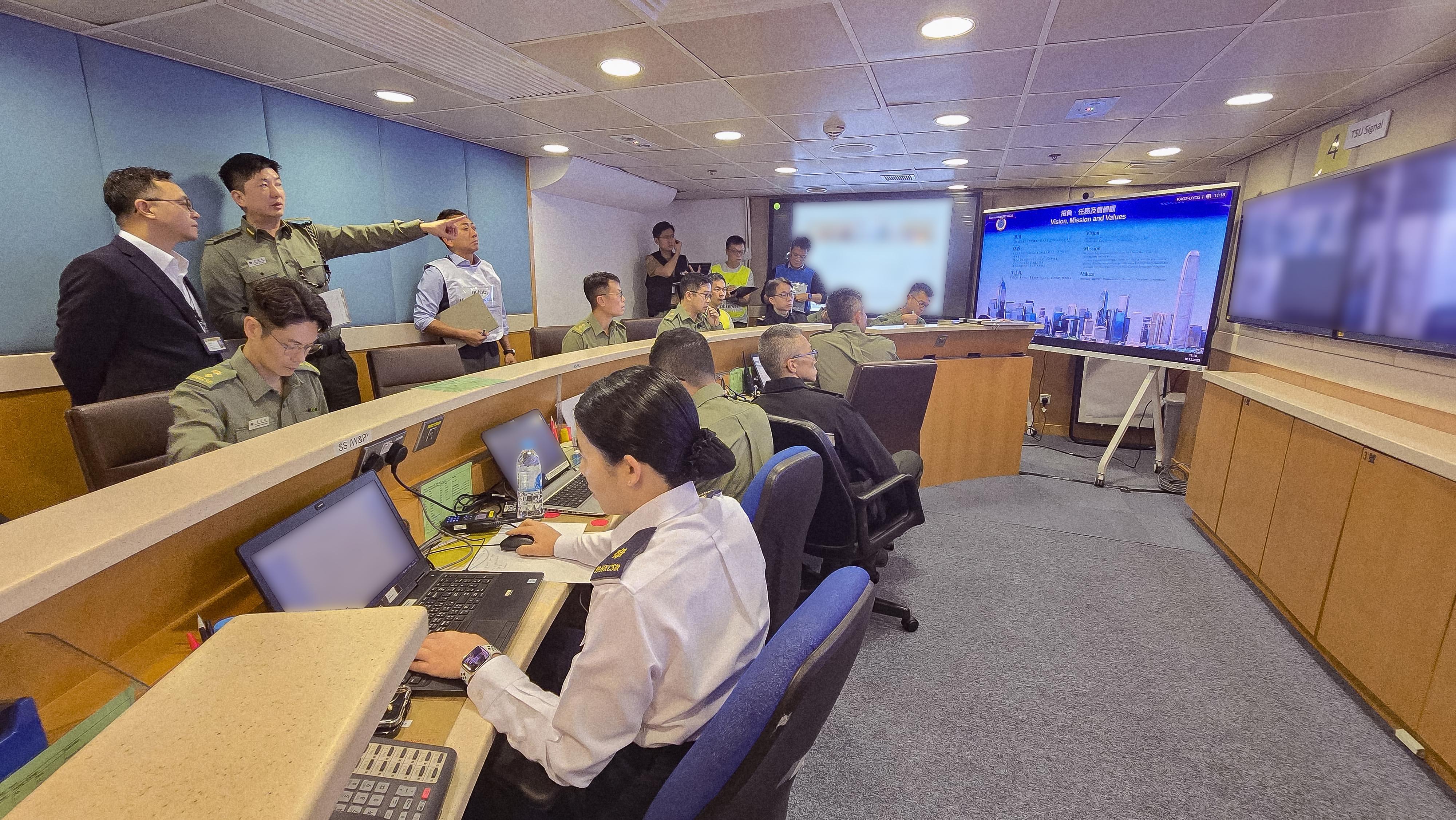 懲教署今日（十二月十日）在喜靈洲懲教所進行代號「和諧二十四號」的大型應變演習，模擬懲教院所發生在囚人士集體騷亂、挾持人質、企圖逃獄、懲教人員遇襲、火警及發現爆炸品等事件。圖示懲教署署長黃國興（後排左一）在演習期間巡視在赤柱的中央控制中心，並聽取懲教署署理助理署長（行動）洪嘉諾（後排左二）匯報應變演習情況。