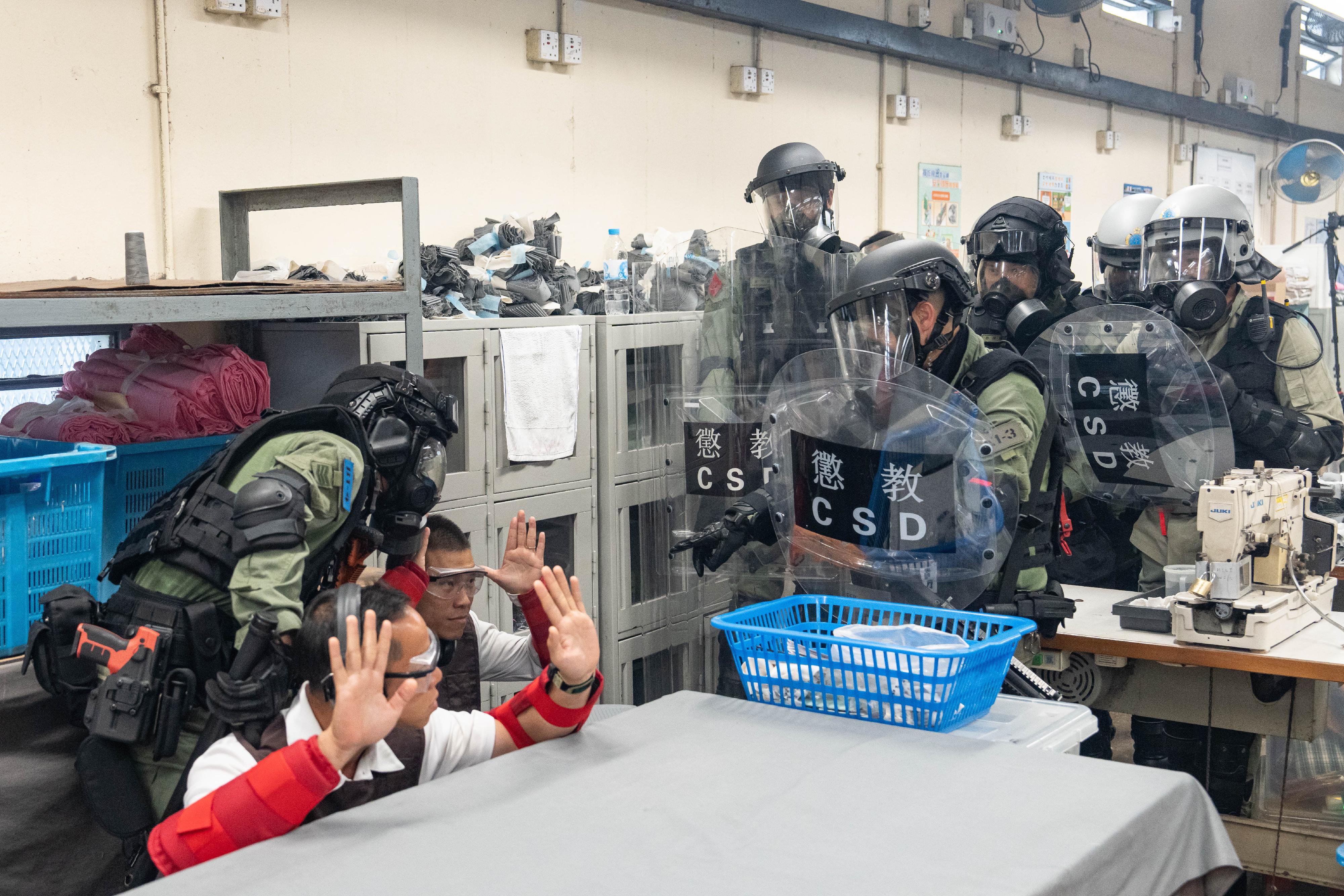 懲教署今日（十二月十日）在喜靈洲懲教所進行代號「和諧二十四號」的大型應變演習，模擬懲教院所發生在囚人士集體騷亂、挾持人質、企圖逃獄、懲教人員遇襲、火警及發現爆炸品等事件。圖示懲教緊急應變隊及區域應變隊人員攻入院所內的工場制服違紀在囚人士。